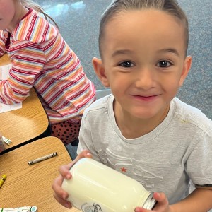 A kindergarten student making butter in a jar.